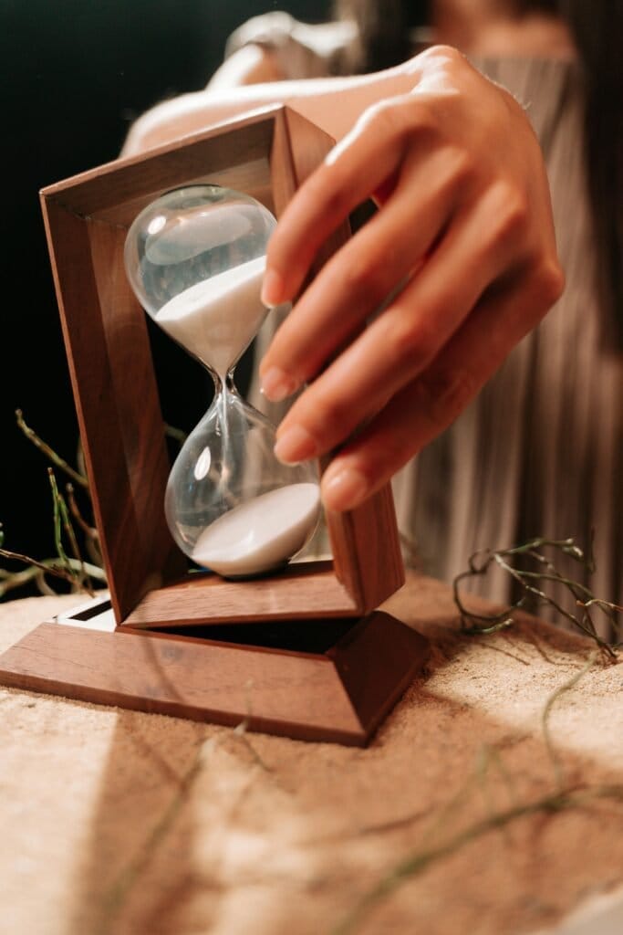 A hand tilting a wooden hourglass, symbolizing the passage of time and countdown.